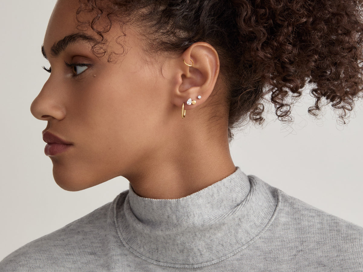 Profile of a woman wearing a gold-tone ear stack: a cartilage hoop, small flat back studs and a lobe hoop