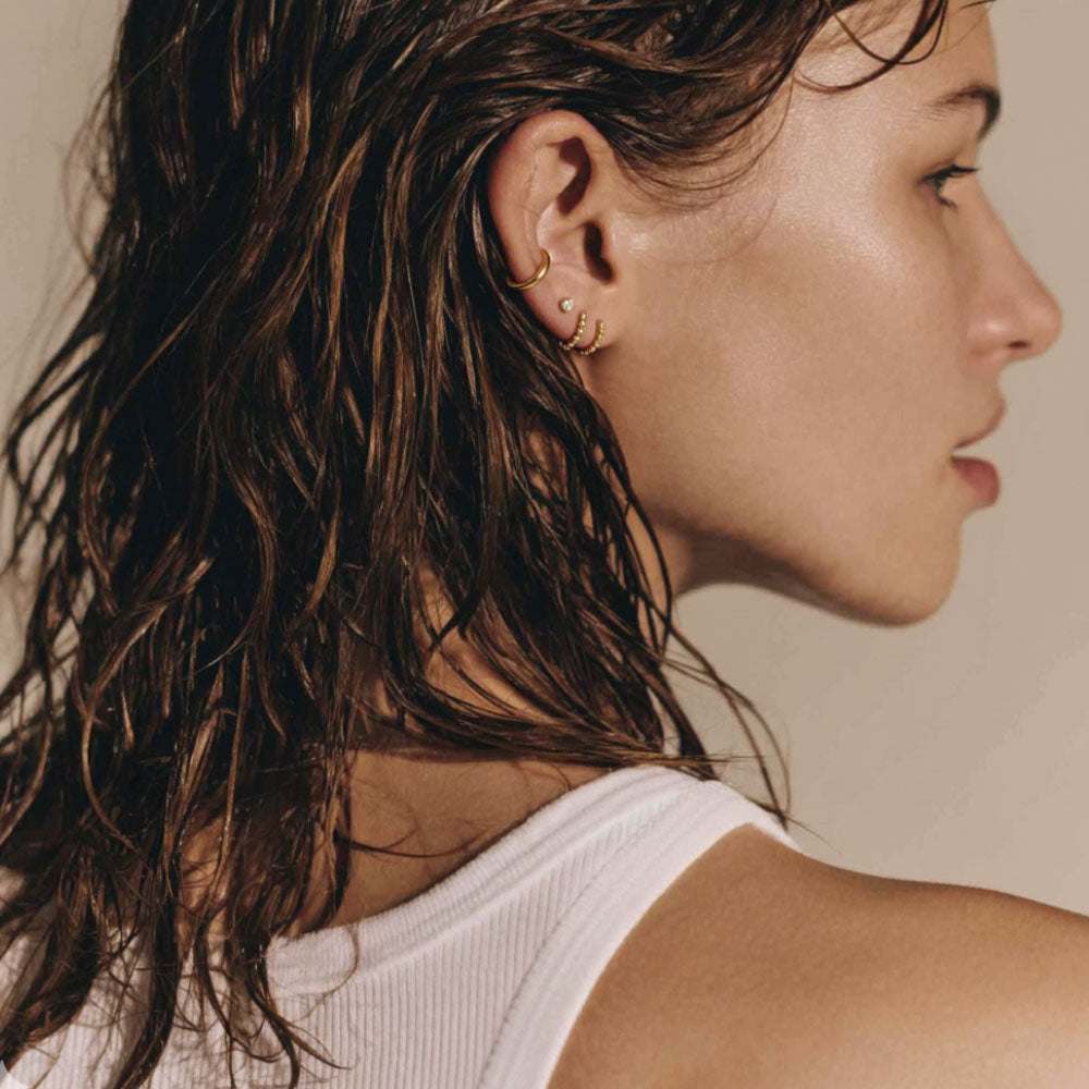Close-up of a woman with wet hair wearing gold earrings against a neutral background