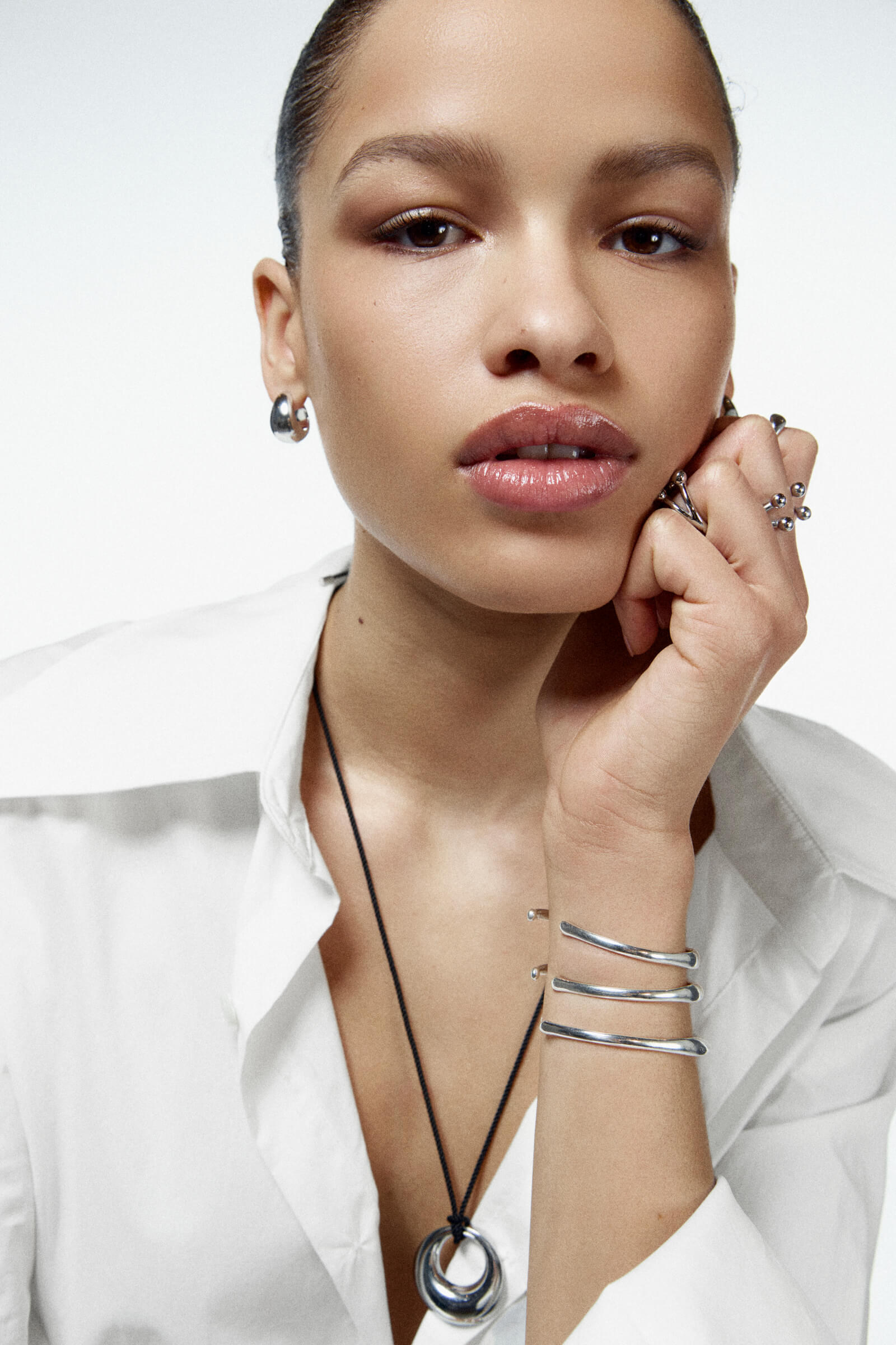 Woman wearing silver jewelry including a necklace, bracelet, and ring on a white background