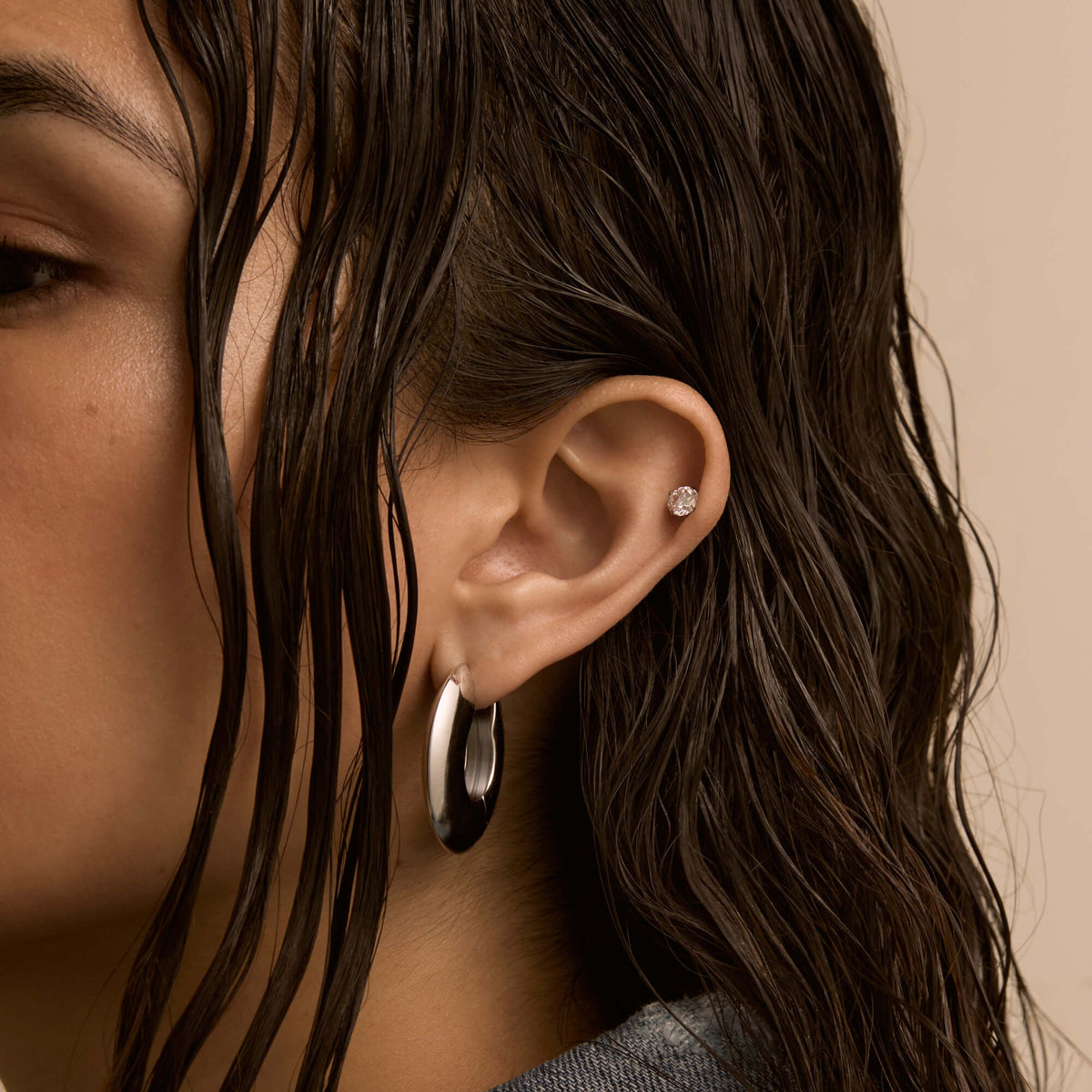 Close-up of an ear with a crystal cartilage stud and a silver-tone lobe hoop