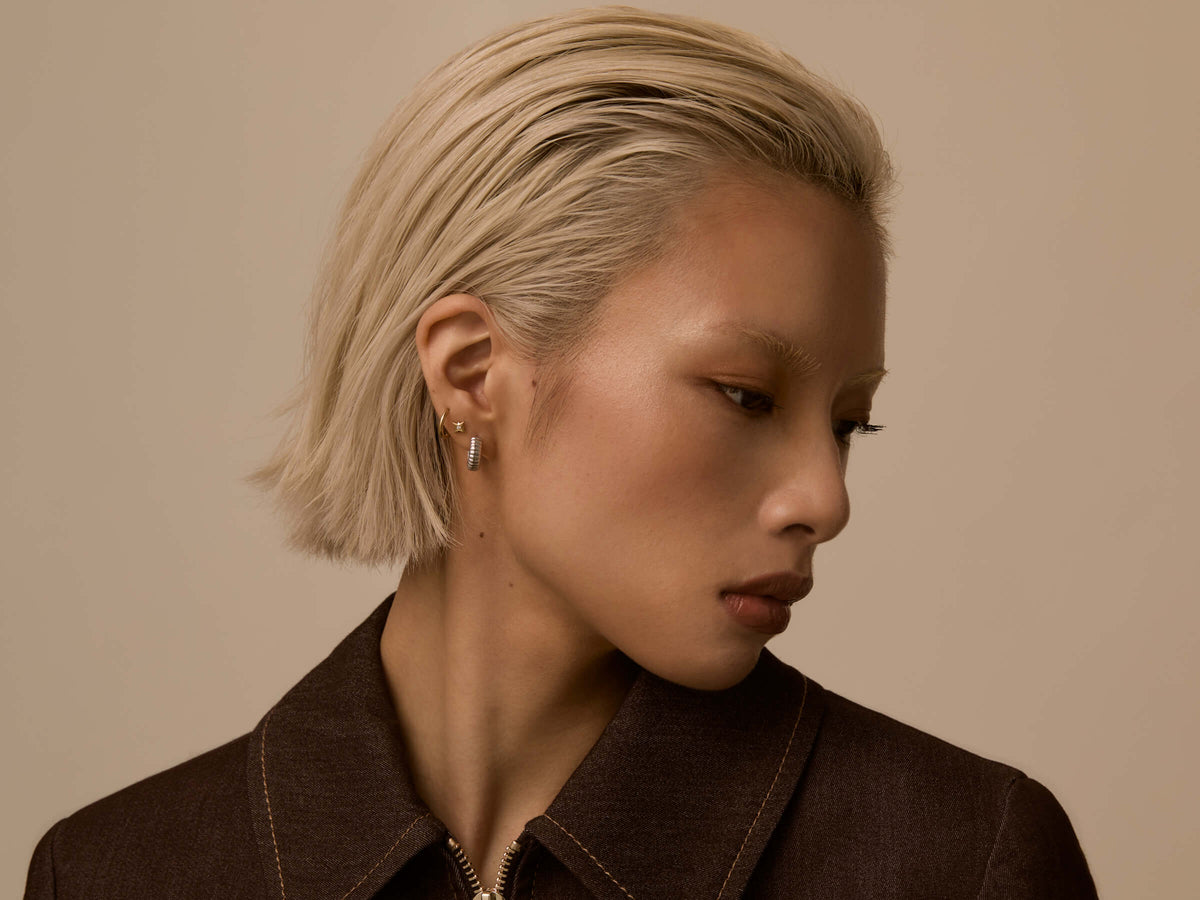 Profile of a woman with a blonde bob wearing a small lobe stack of a stud and a huggie hoop